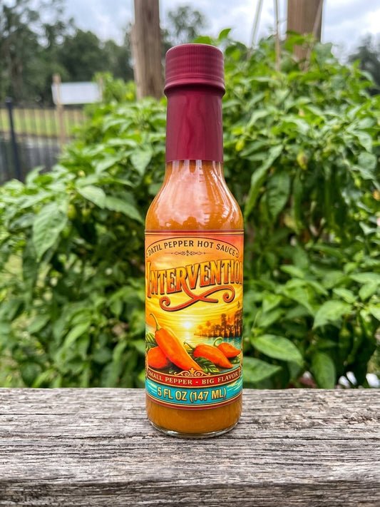 Intervention hot sauce  on a wooden  board and with datil pepper plants in the background.