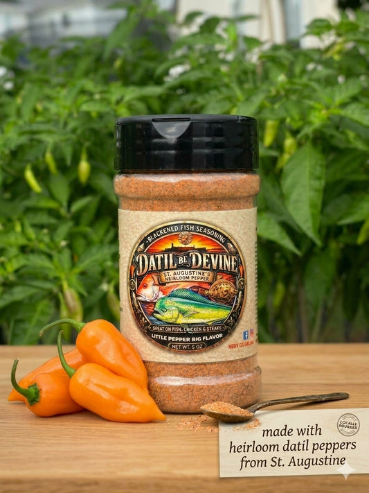 Jar beside peppers: Blackened Seasoning jar beside orange Datil peppers and a spoon of seasoning. Text reads ‘made with heirloom datil peppers from St. Augustine.